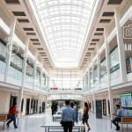 A modern university campus in Tashkent with digital economy symbols like data streams, blockchain icons, and AI interfaces integrated into the architecture, students using tablets and laptops in collaborative spaces, futuristic yet realistic style, bright daylight, high detail
